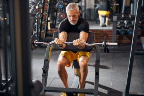 Experienced bodybuilder doing the seated barbell curl exercise on the weight bench at the gym