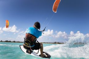 Kitesurfen. Der Surfer steuert mittels Trapez über Leinen einen Lenkdrachen.